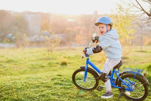 A child in a helmet rides a blue bike on a sunny day
